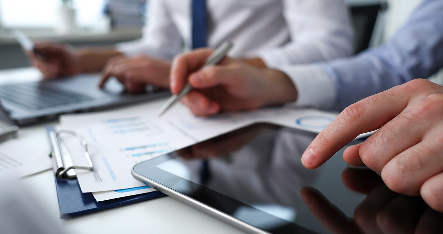 business professionals at a desk using tablet and laptop reviewing charts