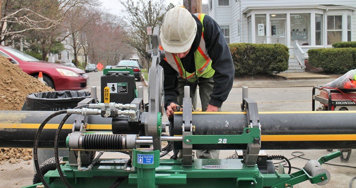 Worker cutting pipe using a large piece of machinery.
